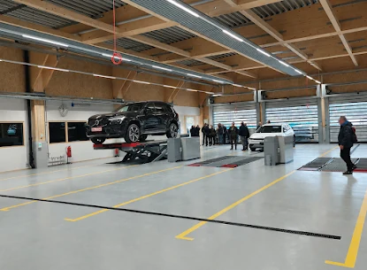 Prüfhalle mit Hebebühne und Prüfstrassen, hinten wartende Personen und Fahrzeuge