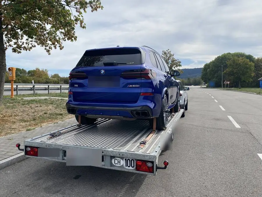 BMW X5 M60i auf dem offenen Anhänger bei einem Halt auf einem Rastplatz in Deutschland, Kontrollschilder unkenntlich gemacht